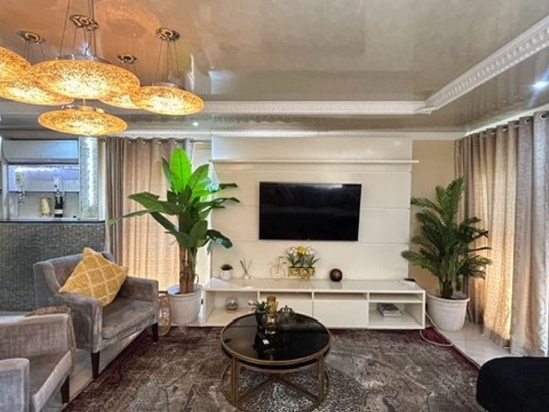 Spacious open-plan living area featuring a modern built-in media wall, decorative ceiling cornice, and a sleek integrated bar counter.