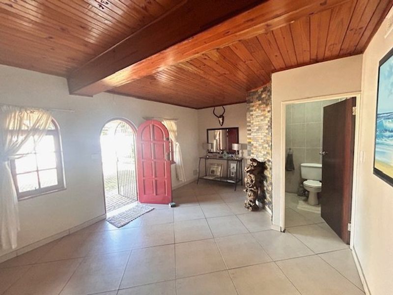 Welcoming entrance hall featuring a timber-clad ceiling, exposed beam, tiled flooring, and a stone-clad feature wall leading to an adjacent bathroom.