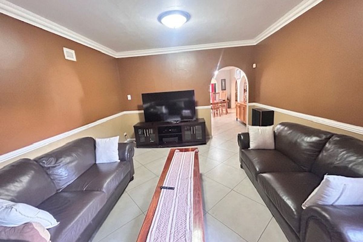 Spacious living room featuring ceramic tile flooring, crown molding, and a decorative chair rail, with an arched entryway leading to the dining area.