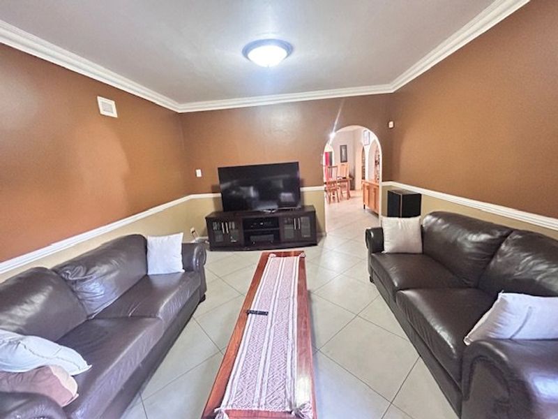 Spacious living room featuring ceramic tile flooring, crown molding, and a decorative chair rail, with an arched entryway leading to the dining area.