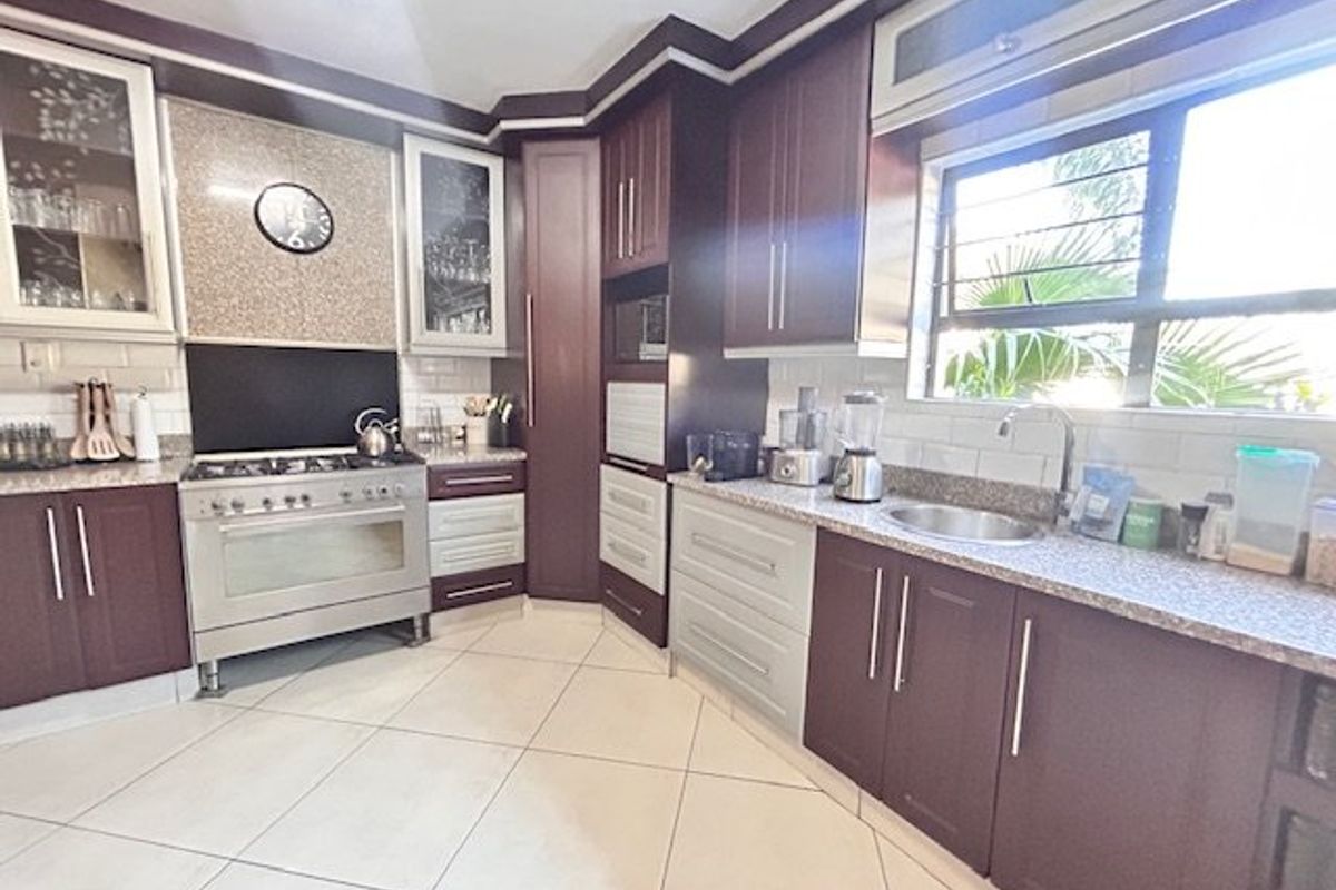 A well-maintained kitchen featuring dark wood cabinetry, granite countertops, a gas stove with extractor, and tiled flooring with ample natural light.