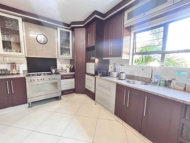 A well-maintained kitchen featuring dark wood cabinetry, granite countertops, a gas stove with extractor, and tiled flooring with ample natural light.