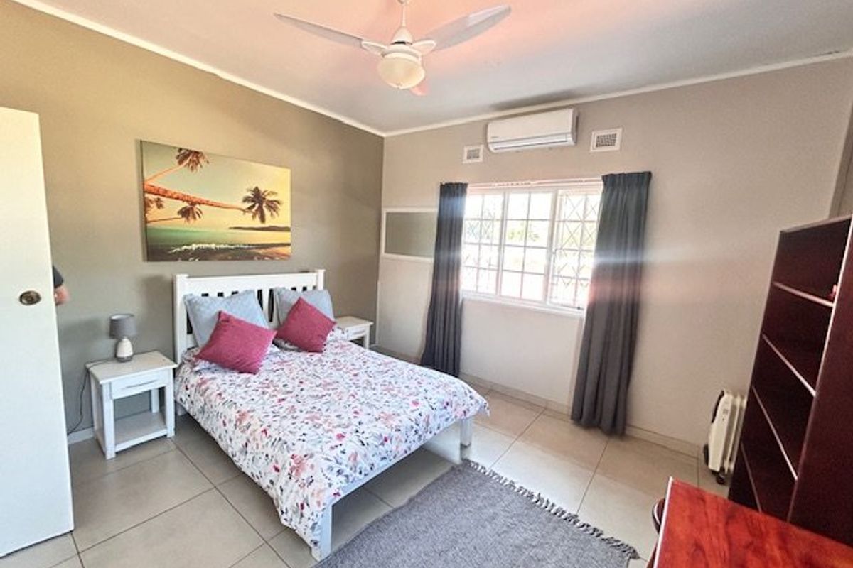 A well-maintained bedroom featuring tiled flooring, a ceiling fan, and a wall-mounted split-system air conditioner for climate control.