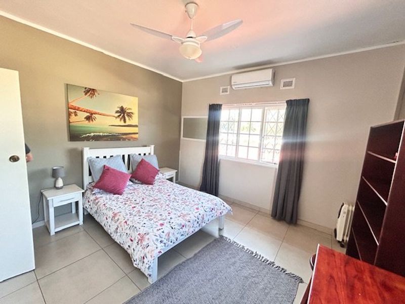 A well-maintained bedroom featuring tiled flooring, a ceiling fan, and a wall-mounted split-system air conditioner for climate control.