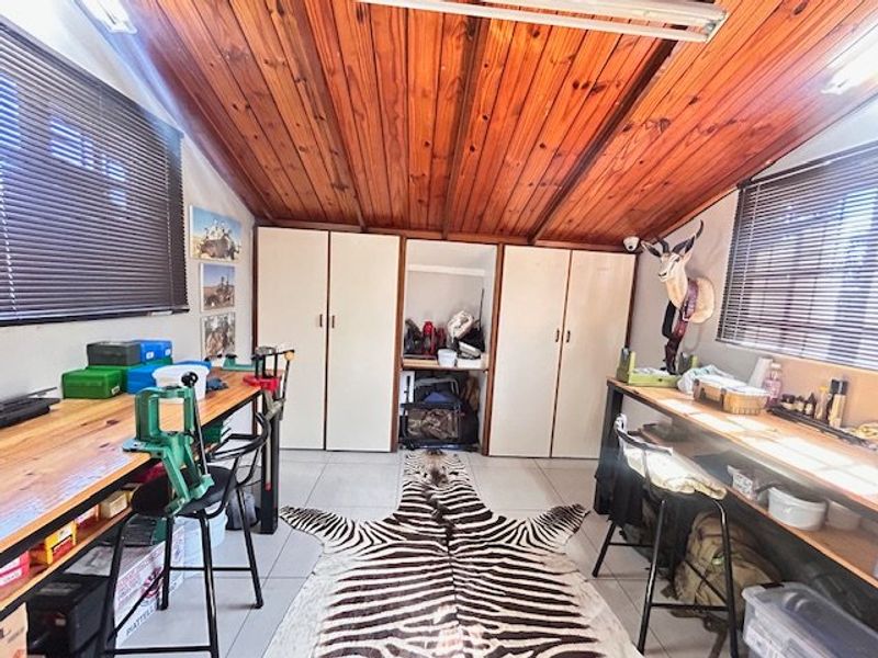 A functional utility space or workshop featuring a timber-clad vaulted ceiling, tiled flooring, and extensive built-in cabinetry for storage.