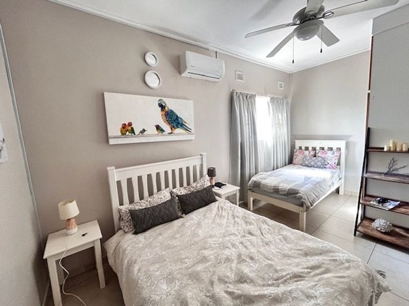 A well-maintained bedroom featuring tiled flooring, a ceiling fan, and a wall-mounted split-system air conditioner.