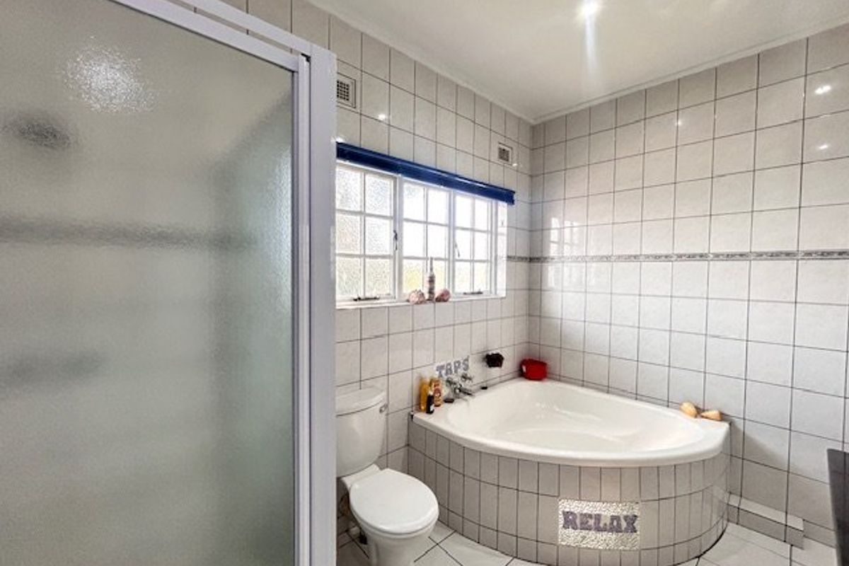 A functional bathroom featuring a corner bathtub, separate shower enclosure, and tiled finishes throughout.