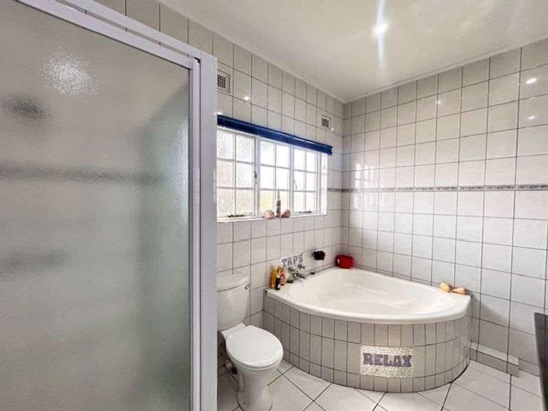 A functional bathroom featuring a corner bathtub, separate shower enclosure, and tiled finishes throughout.