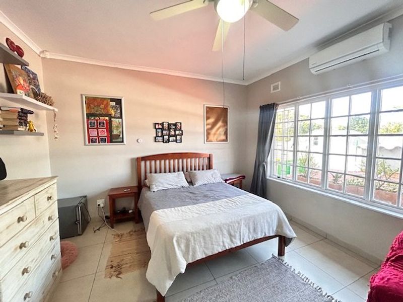A well-lit bedroom featuring tiled flooring, a ceiling fan, and a wall-mounted split-system air conditioner for climate control.