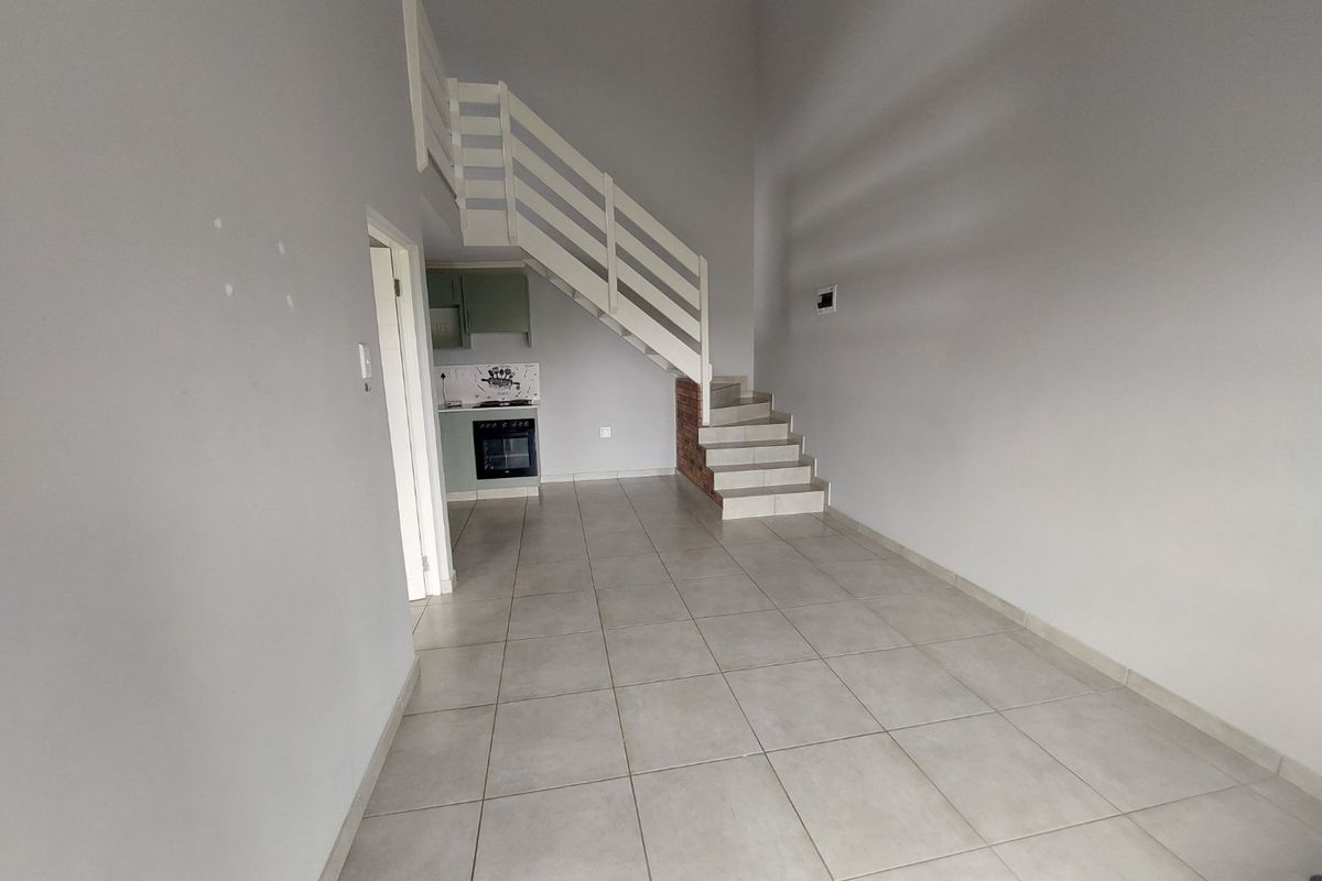An open-plan living area featuring tiled flooring, a staircase, and a compact kitchen with built-in oven and hob.