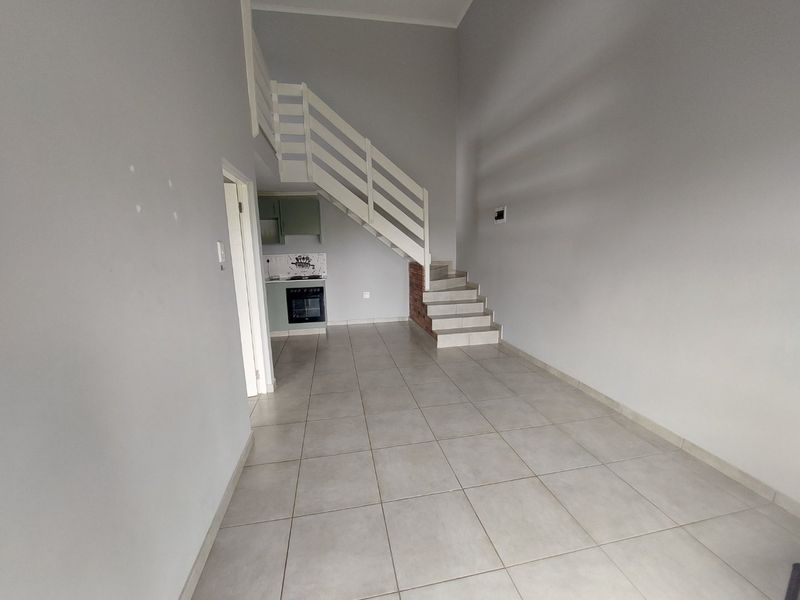 An open-plan living area featuring tiled flooring, a staircase, and a compact kitchen with built-in oven and hob.