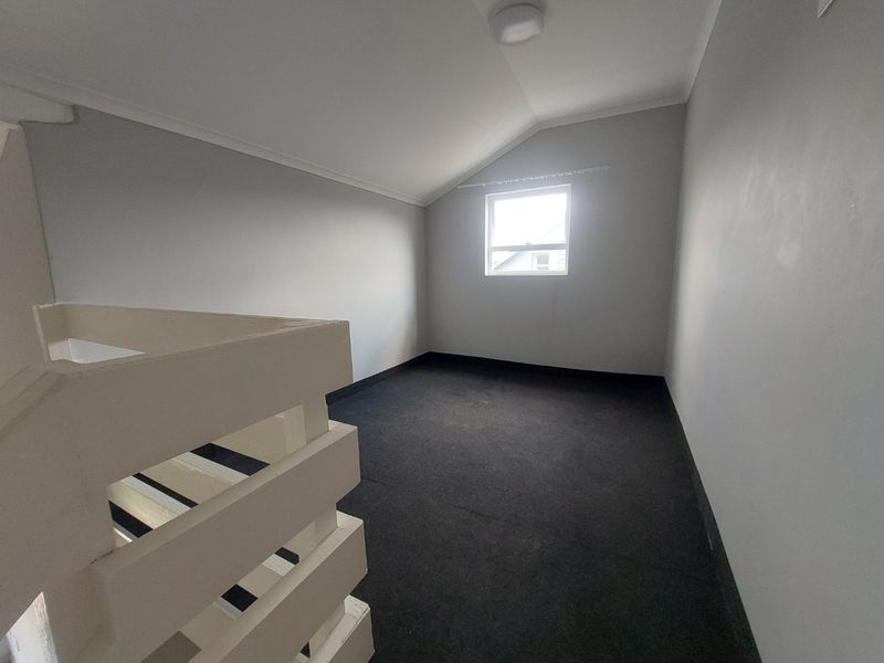 An empty bedroom featuring a sloped ceiling, dark carpeting, and a wooden balustrade overlooking the lower level.