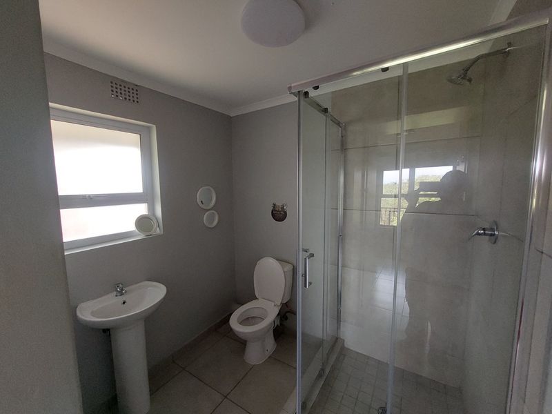 A clean and functional bathroom featuring a pedestal basin, a toilet, and a glass-enclosed shower with tiled flooring.
