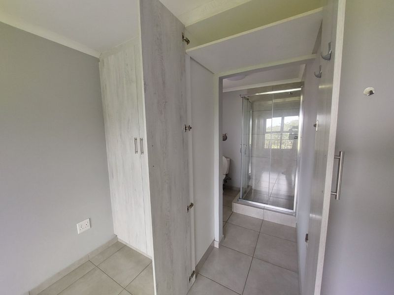 A clean bedroom area featuring built-in cupboards and direct access to an en-suite bathroom with a glass shower enclosure.
