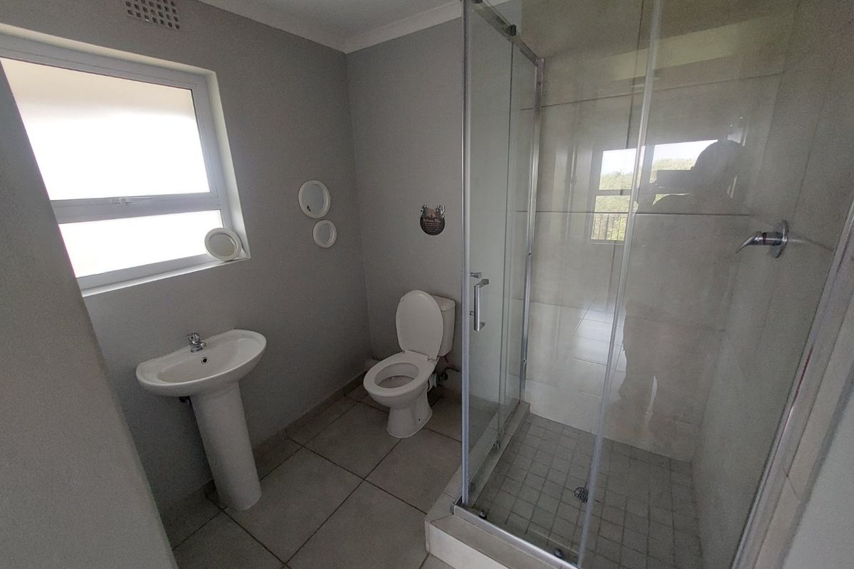 A clean and functional bathroom featuring a pedestal basin, a toilet, and a glass-enclosed shower with neutral floor and wall tiling.