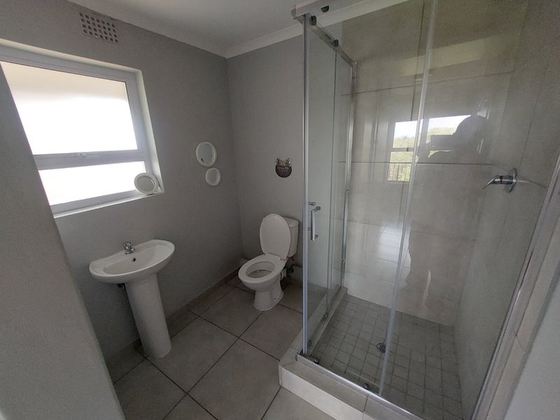 A clean and functional bathroom featuring a pedestal basin, a toilet, and a glass-enclosed shower with neutral floor and wall tiling.