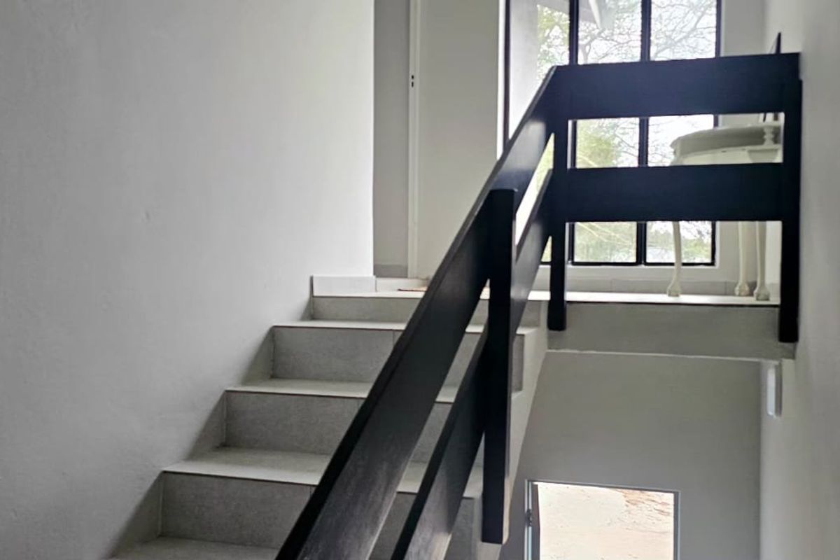 A simple interior staircase featuring tiled treads and a dark timber handrail, leading to an upper landing with natural light.