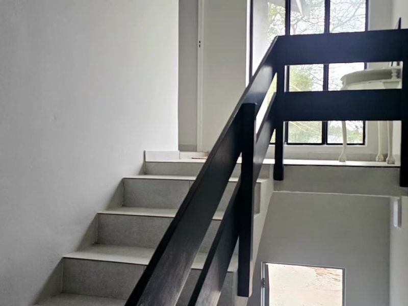 A simple interior staircase featuring tiled treads and a dark timber handrail, leading to an upper landing with natural light.