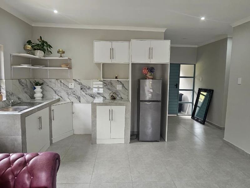 Open-plan kitchen and living area featuring modern marble-look backsplash, built-in cabinetry, tiled flooring, and ample natural light from large windows.