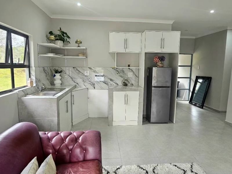 Open-plan living area featuring a compact kitchen with marble-look backsplash, built-in cabinetry, and neutral tiled flooring throughout.