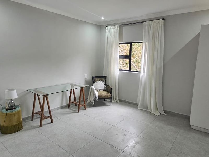 A well-lit bedroom featuring neutral tiled flooring, a built-in wardrobe, and a window with curtain rails, offering a clean and functional living space.