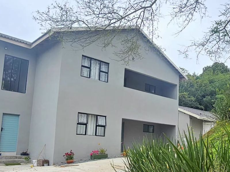 A modern two-story residential building featuring a neutral grey facade, aluminium window frames, and a covered balcony area.