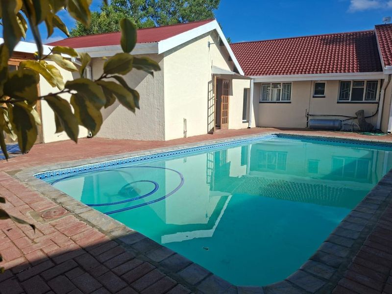 A backyard pool area featuring brick paving, a swimming pool, and views of the rear building elevation with tiled roofing.