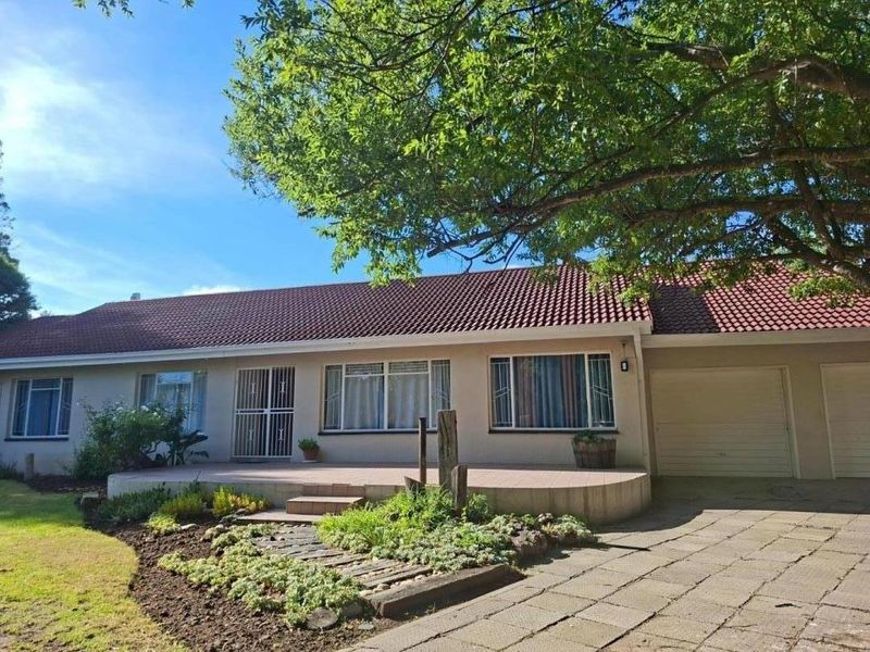 A well-maintained single-story house featuring a tiled roof, paved driveway, attached garage, and a welcoming front patio set within a landscaped garden.