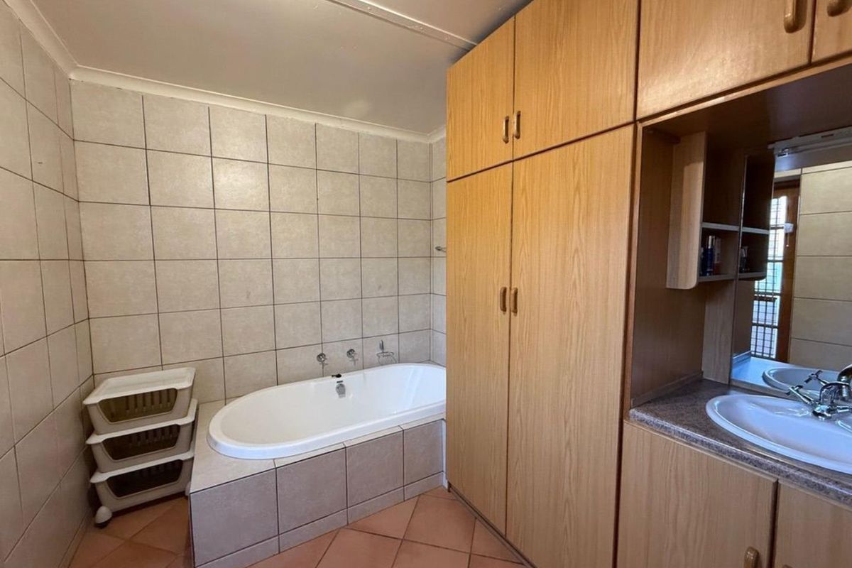 A functional bathroom featuring a built-in bathtub with tiled surround, extensive wooden cabinetry, and a vanity with an integrated basin.