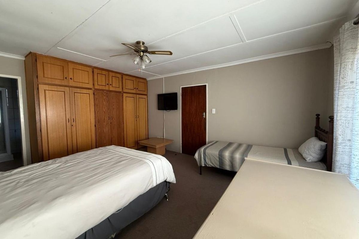 A spacious bedroom featuring extensive built-in wooden cupboards, a ceiling fan, and neutral wall finishes.