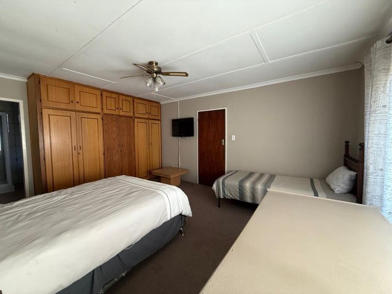 A spacious bedroom featuring extensive built-in wooden cupboards, a ceiling fan, and neutral wall finishes.