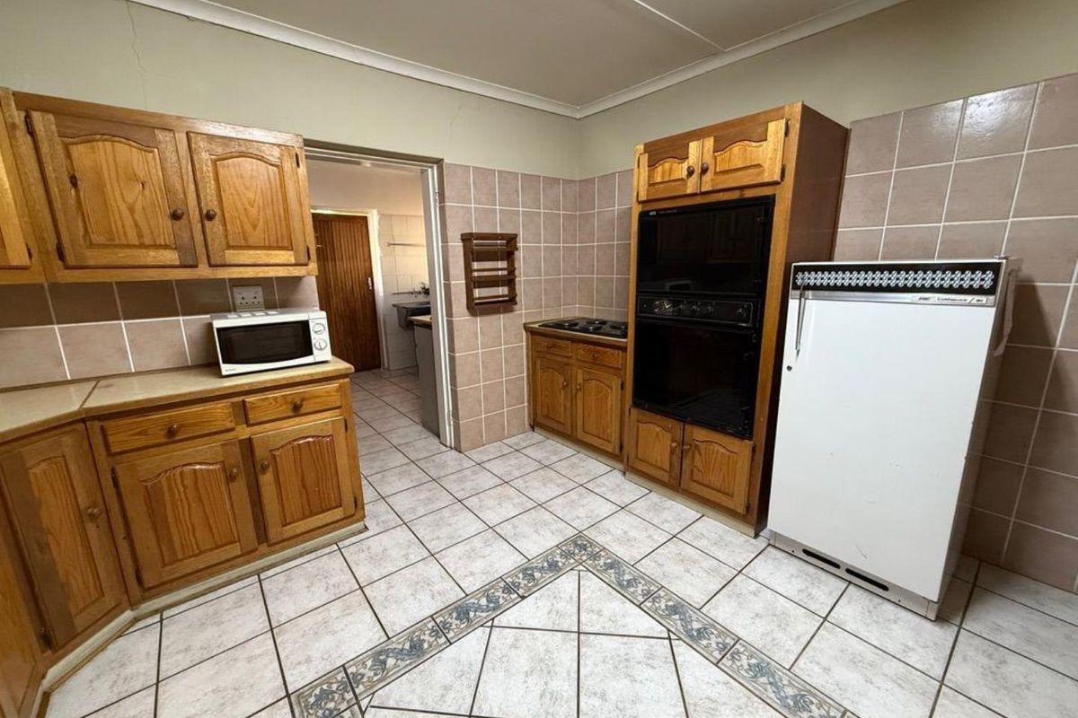 A dated kitchen featuring wooden cabinetry, tiled flooring with decorative inlay, and built-in oven and hob, offering potential for modern renovation.