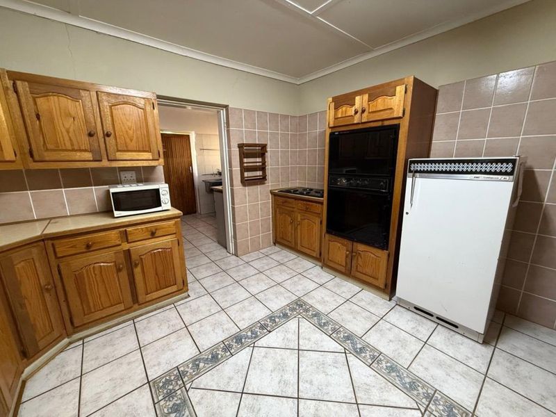 A dated kitchen featuring wooden cabinetry, tiled flooring with decorative inlay, and built-in oven and hob, offering potential for modern renovation.