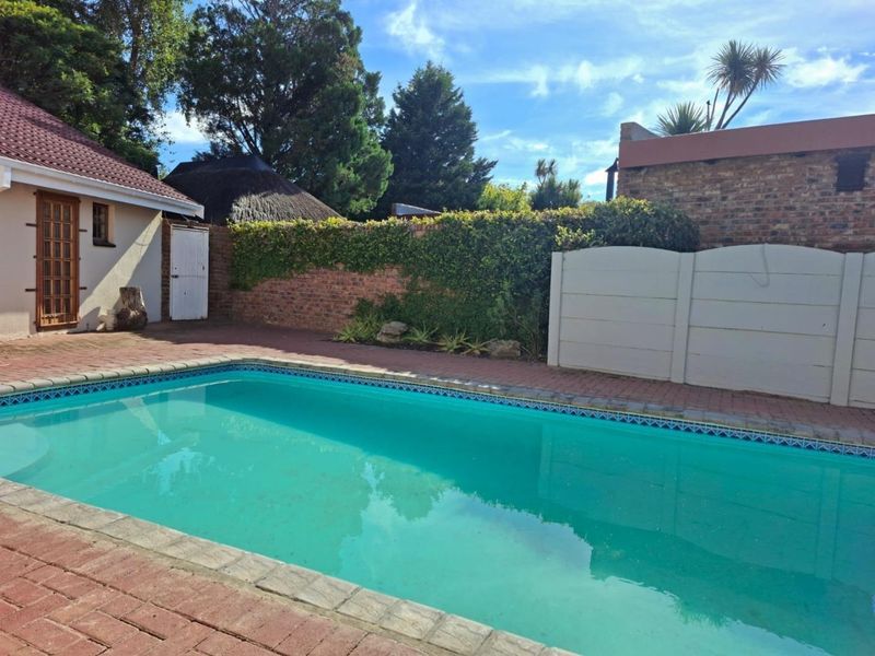 Outdoor pool area featuring a swimming pool with brick paving, enclosed by a combination of brick and precast concrete boundary walls.