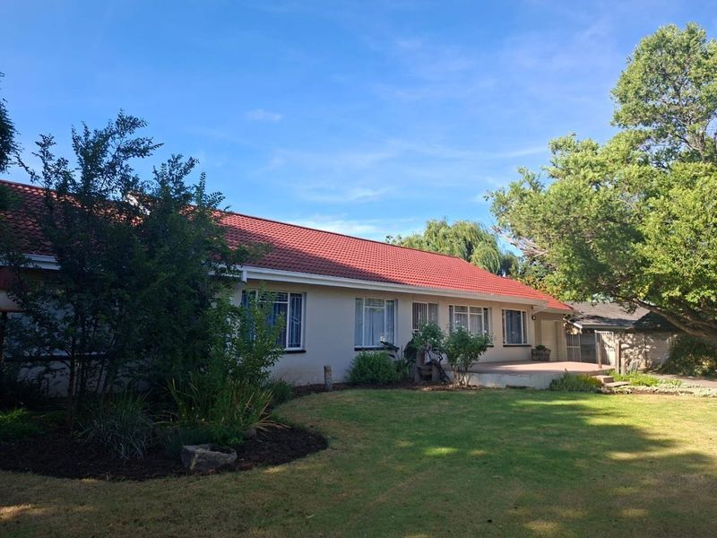 Rear view of the house featuring a tiled roof, a paved patio area, and a well-maintained garden.