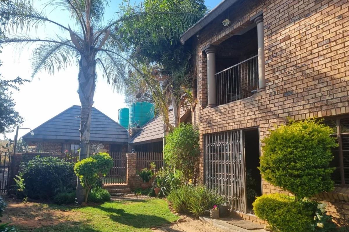Rear view of a face brick commercial property featuring a landscaped garden, upper-level balcony, and integrated water storage tanks.