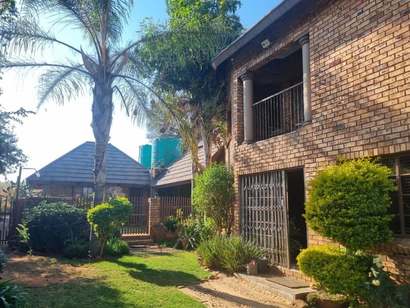 Rear view of a face brick commercial property featuring a landscaped garden, upper-level balcony, and integrated water storage tanks.