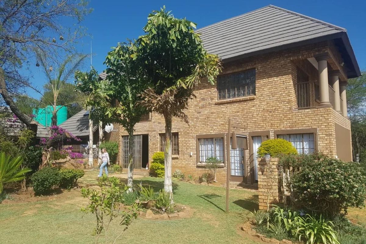 A two-story face brick commercial property featuring a tiled roof, security bars on windows, and an upper-level balcony overlooking a landscaped garden area.