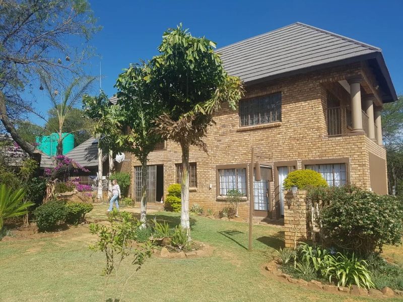 A two-story face brick commercial property featuring a tiled roof, security bars on windows, and an upper-level balcony overlooking a landscaped garden area.