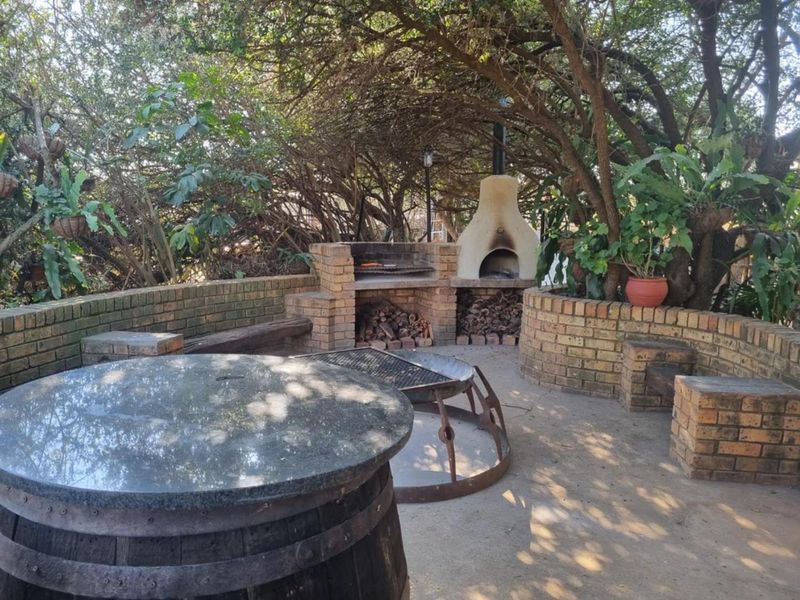 Outdoor entertainment area featuring a built-in brick braai and pizza oven, set within a shaded garden space with brick retaining walls.