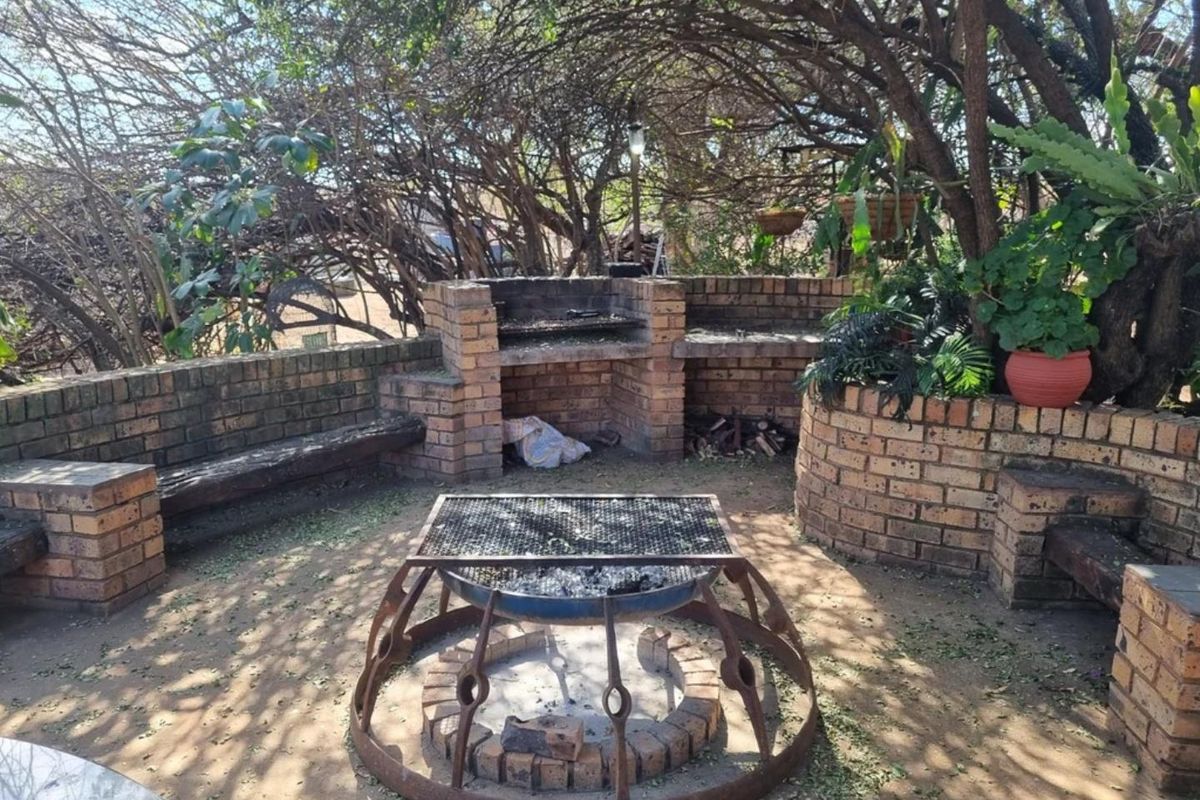 Outdoor entertainment area featuring a built-in brick braai, integrated brick seating, and a central fire pit under mature tree canopy.