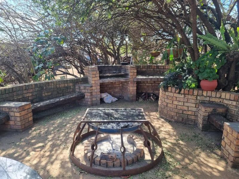 Outdoor entertainment area featuring a built-in brick braai, integrated brick seating, and a central fire pit under mature tree canopy.