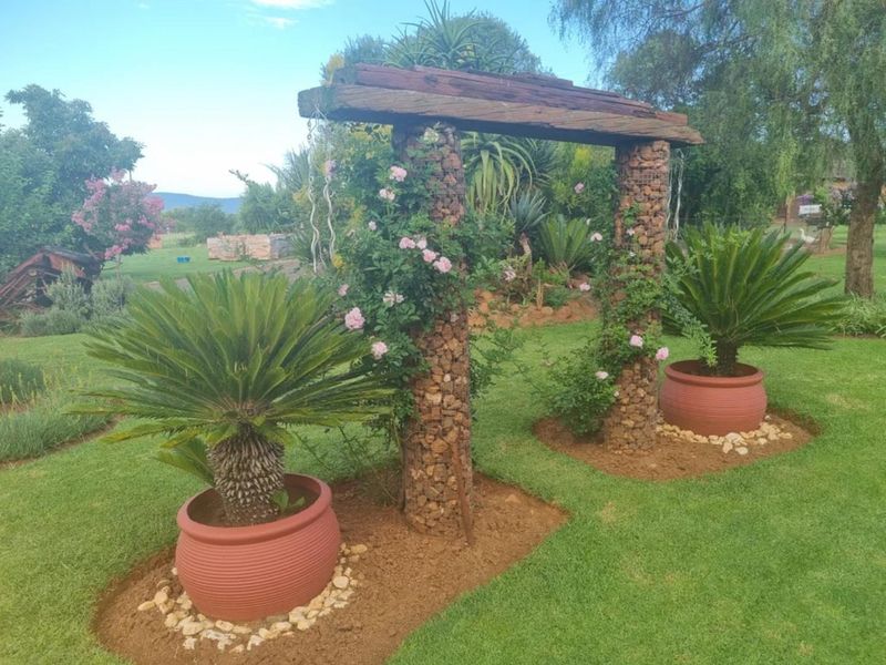 A well-maintained garden area featuring a decorative timber and gabion stone archway set within a landscaped lawn.