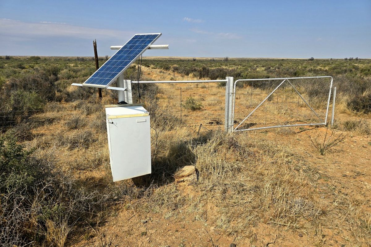 A remote farm gate entrance featuring a solar-powered utility system and wire fencing set within an open landscape.