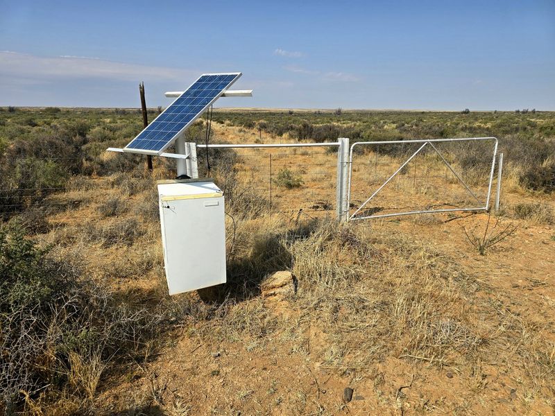 A remote farm gate entrance featuring a solar-powered utility system and wire fencing set within an open landscape.