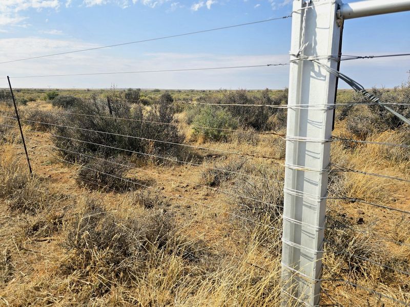 A view of the expansive farm landscape featuring wire fencing and a sturdy metal fence post.