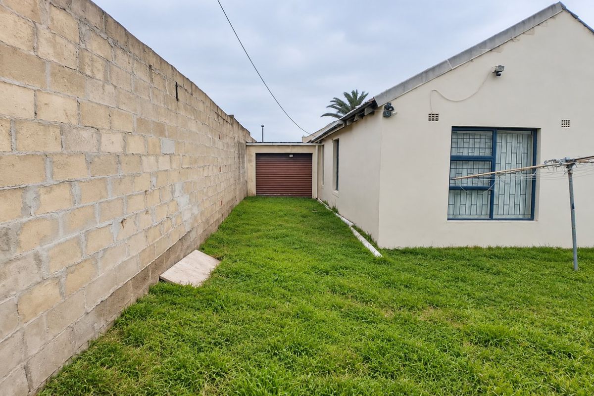 Rear exterior view showing a grassed yard, boundary wall, and access to a single garage with a roller door.