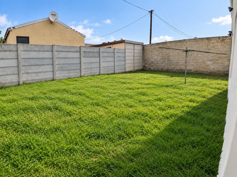 A private rear garden featuring a lawn area, enclosed by a combination of precast concrete and masonry boundary walls.