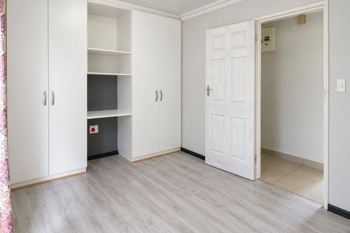 A clean, empty bedroom featuring modern laminate flooring, built-in white cabinetry with integrated shelving, and a panelled ceiling.
