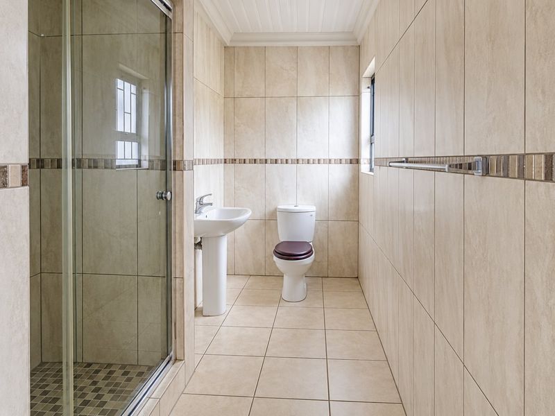 A clean, neutral-toned bathroom featuring a glass shower enclosure, pedestal basin, and toilet with full-height wall tiling.